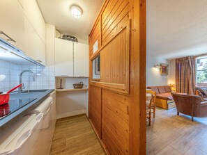 A compact kitchen with white cabinets, a stainless steel sink, and a red pot. Adjacent is a wooden-paneled room with a sofa and a window. - Classic Apartment with Wifi, 2 BR, Val-d'Isère (Val-d'Isère)