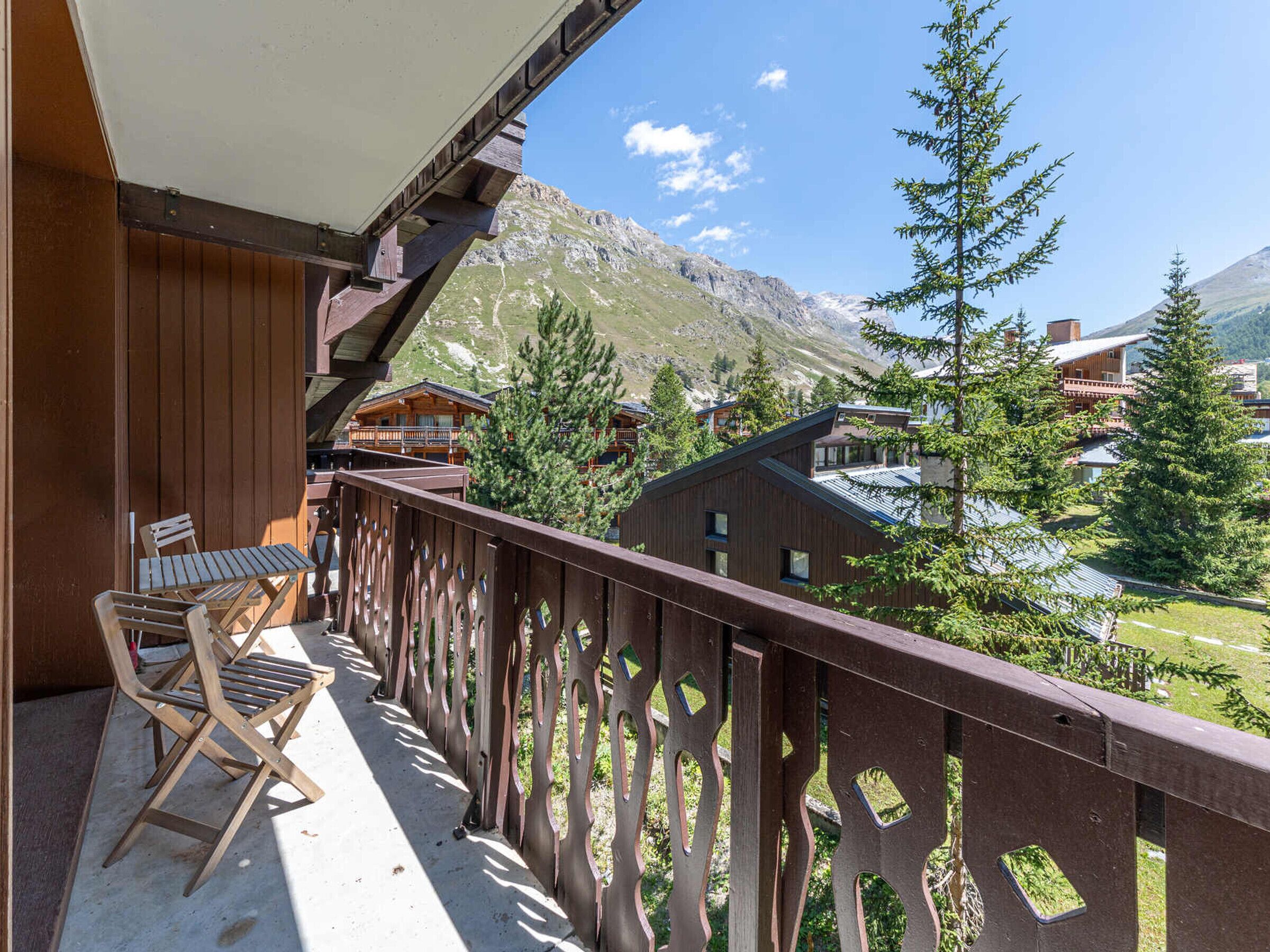 A balcony with wooden railings overlooking a mountainous landscape and a row of wooden buildings.