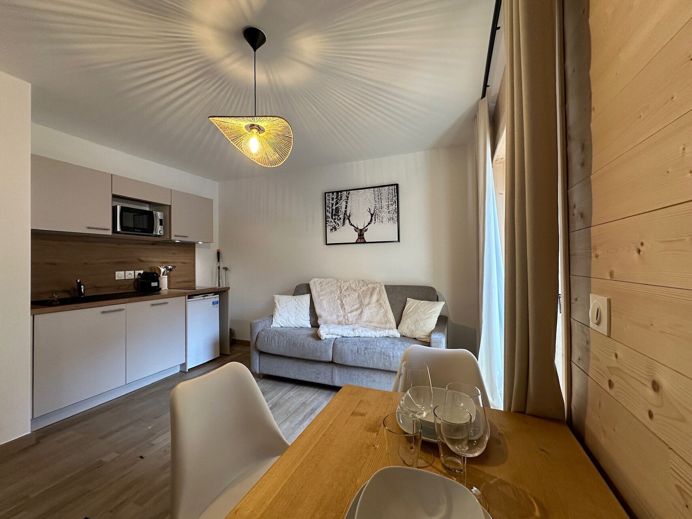 A modern kitchen with a microwave, a dining table with glasses and a plate, and a grey sofa with cushions.