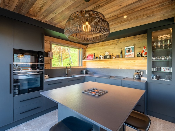 A modern kitchen with a central island, built-in appliances, and a wooden ceiling.