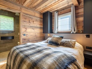 Une chambre avec un plafond en bois, un lit recouvert d’une couverture à rayures, une fenêtre avec des rideaux et un luminaire fixé au mur.