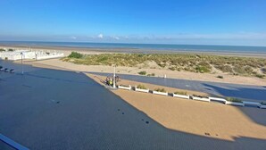 A beachside promenade with a paved walkway, a bike lane, and a view of the beach and dunes.
