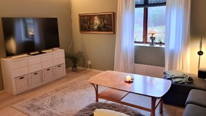 Ett vardagsrum med en tv, en tavla, ett fönster med gardiner, ett bord och en soffa.