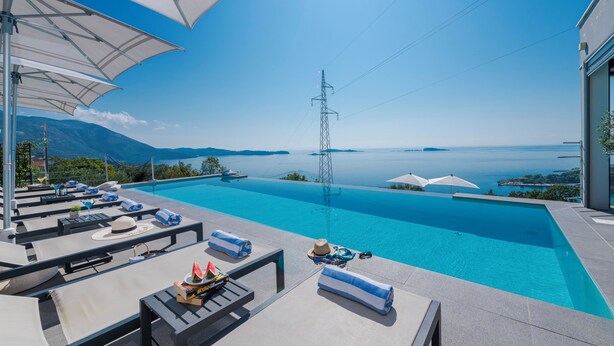 Ein Poolbereich mit Liegestühlen, Sonnenschirmen und Blick auf das Meer.