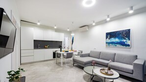 Ein modernes Wohnzimmer mit einem grauen Sofa, einem runden Couchtisch und einem Essbereich mit einem weißen Tisch und Stühlen.
