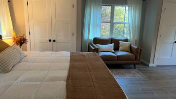 Quarto com cama grande, sofá marrom e janela com cortinas.