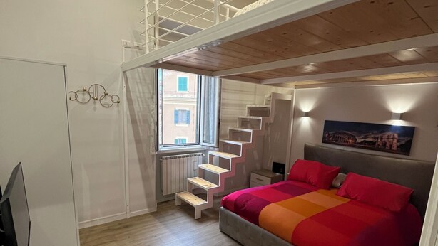 A bedroom with a bed, a desk, a chair, a window, and a staircase. - Apartment Rome center (Roma)