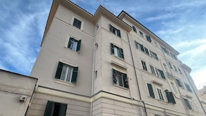 A multi-story building with a beige facade, multiple windows with green shutters, and a visible door. - Apartment Rome center (Roma)