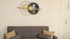 Ein modernes Wohnzimmer mit einem grauen Sofa, einem runden weißen Couchtisch und einem petrolfarbenen Ottomanen.