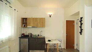 Eine kleine Küche mit Kühlschrank, Spüle und Holzschränken. Ein Esstisch mit Stühlen und einer Wandleuchte sind ebenfalls vorhanden.