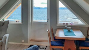 A room with a view of the sea, a dining table with chairs, a sofa, and a small rug. - 3 Person Holiday Home in Tranoy (Hamaroy)