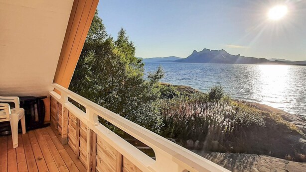 A wooden deck with a white railing overlooking a body of water and distant mountains. - 3 Person Holiday Home in Tranoy (Hamaroy)