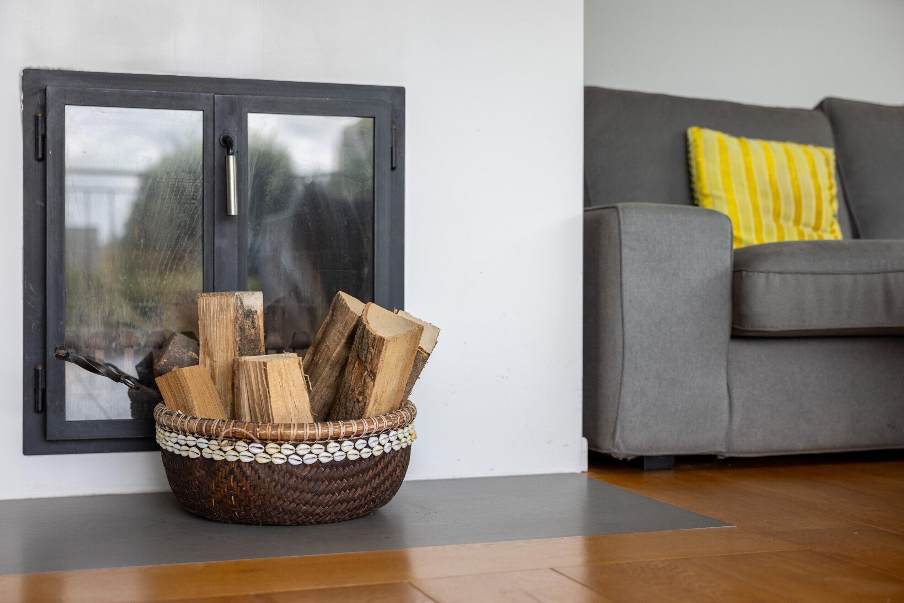 Ein Zimmer mit einem grauen Sofa, einem gelb gestreiften Kissen und einem Holzkorb vor einer weißen Wand.