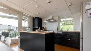 Una cocina moderna con una isla central, muebles de color negro, electrodomésticos de acero inoxidable y amplias ventanas que permiten la entrada de luz natural.