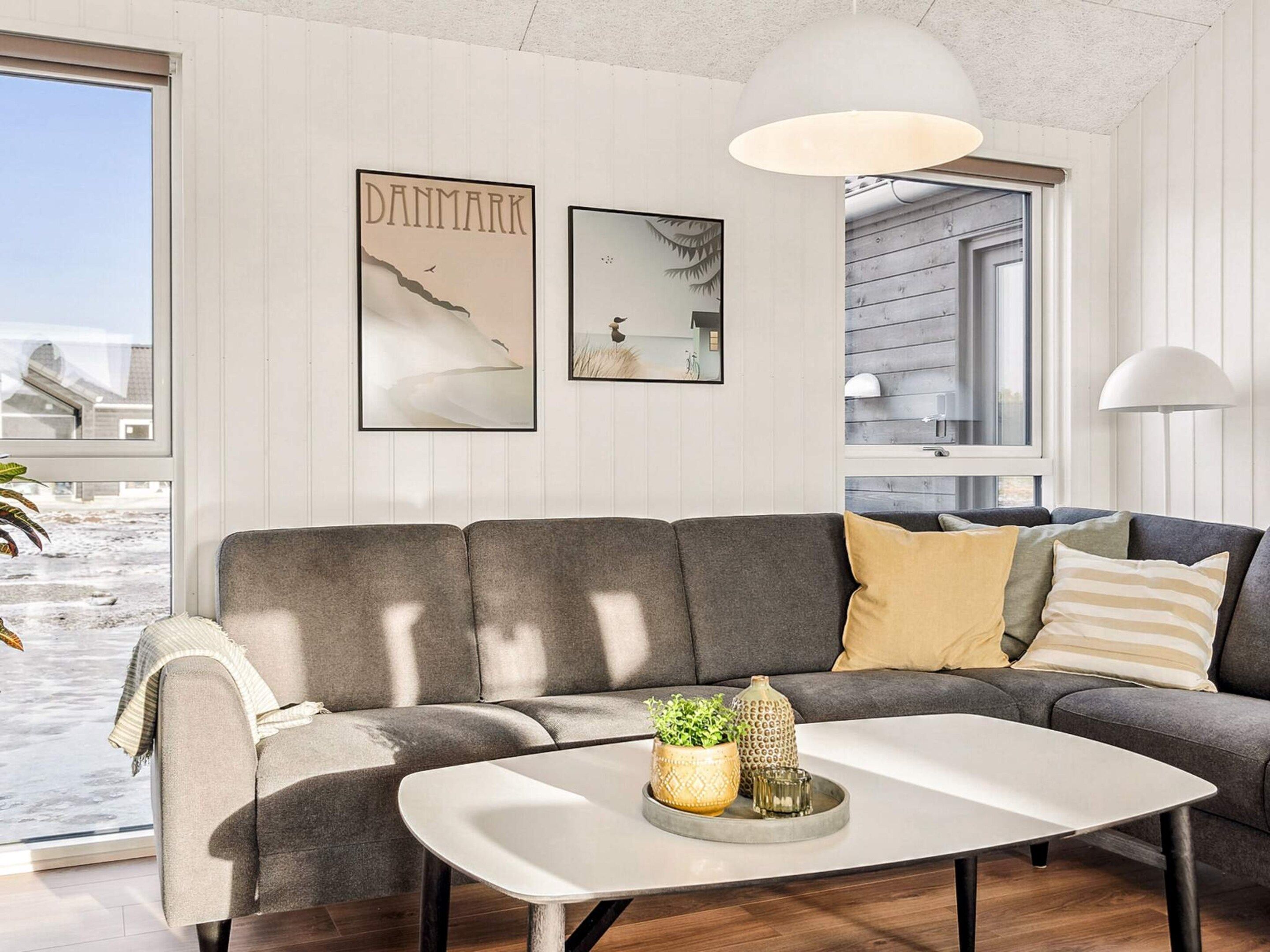 A modern living room with a grey sectional sofa, a white coffee table, and decorative items. There are two framed pictures on the wall, one of a landscape and another of a bird.