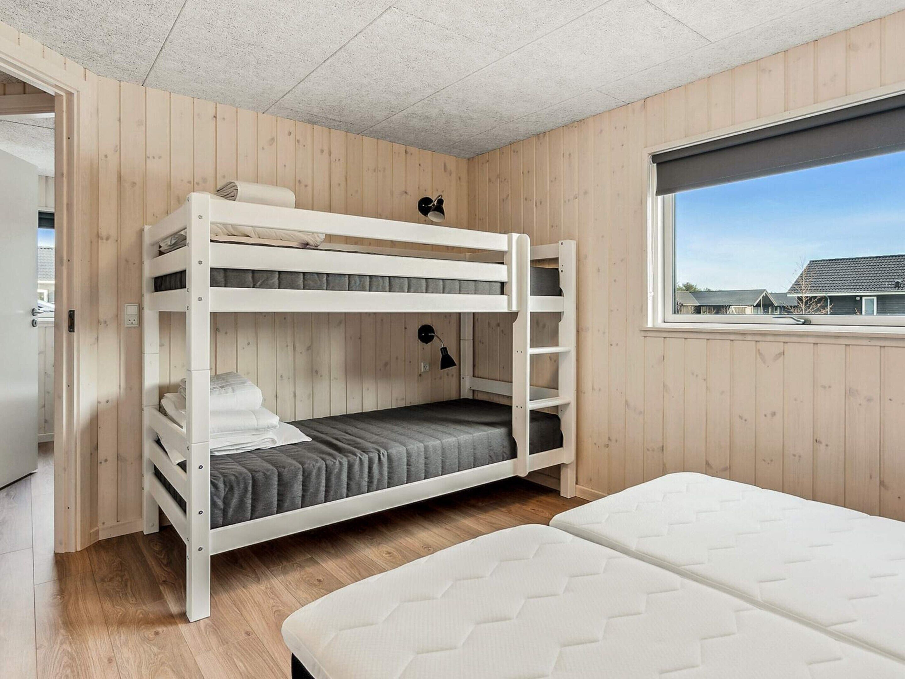 Habitación con literas, ventana, paredes de madera y una puerta.