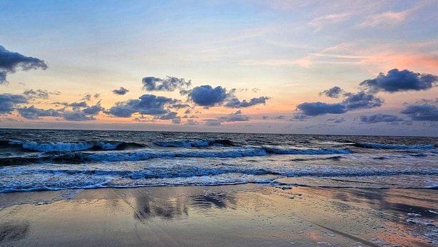 Una playa con olas, cielo despejado y nubes dispersas.