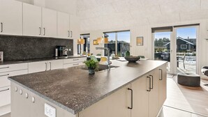 Una cocina moderna con una isla grande, armarios blancos y vistas al exterior.