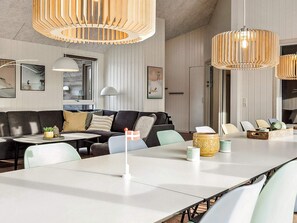 A modern interior with a long dining table, a sofa, and pendant lighting. - 5 Star Holiday Home in Norre Nebel (Norre Nebel)