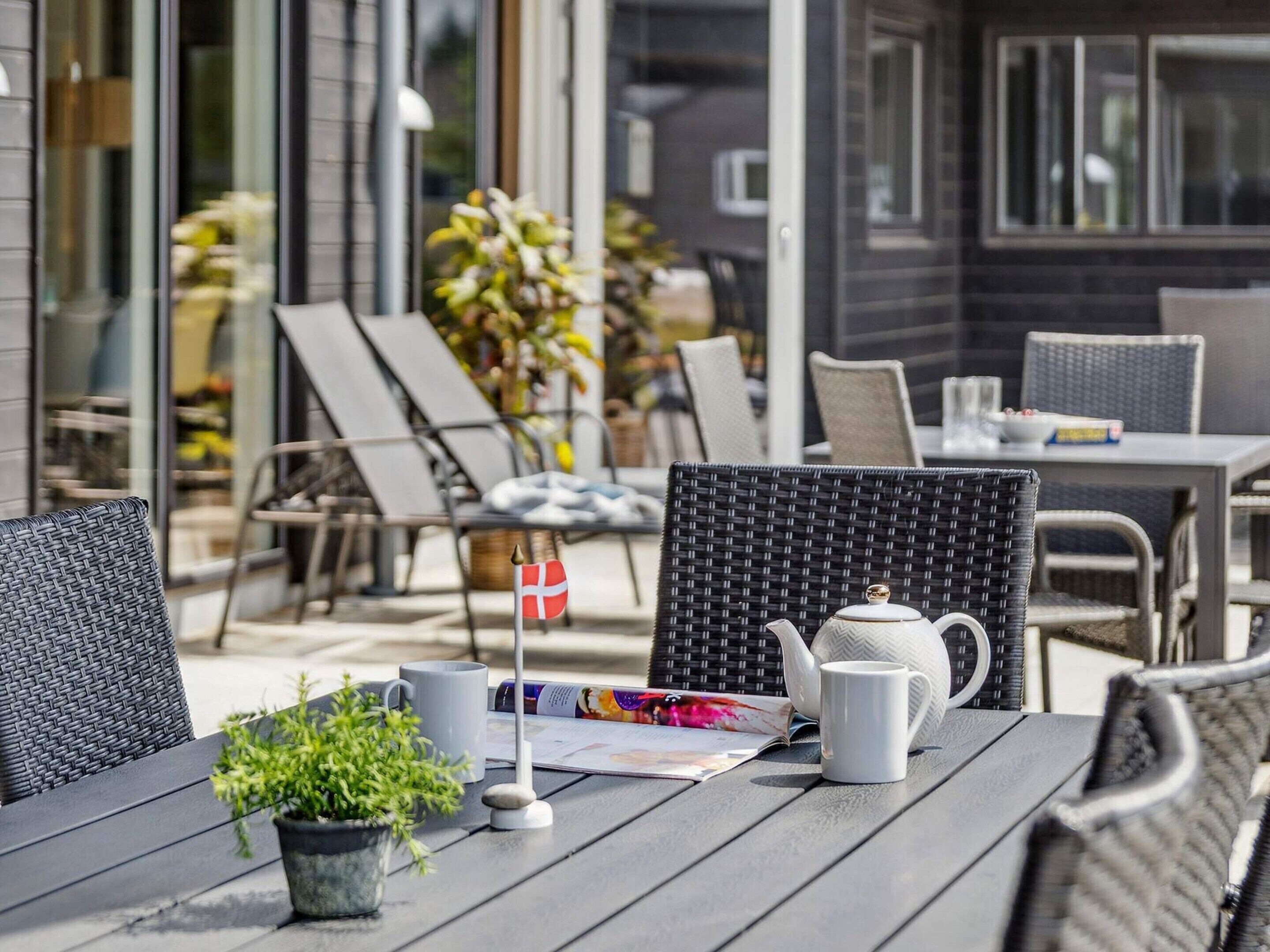 A patio with outdoor seating, a table with a teapot, a potted plant, and a magazine.