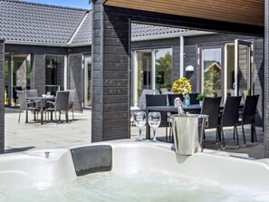 A hot tub with two glasses and a champagne bottle, surrounded by outdoor furniture and a patio area. - 5 Star Holiday Home in Norre Nebel (Norre Nebel)