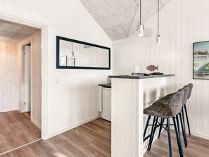A modern kitchen with a wooden floor, white cabinetry, a bar area with stools, pendant lighting, and a framed picture on the wall. - 5 Star Holiday Home in Norre Nebel (Norre Nebel)