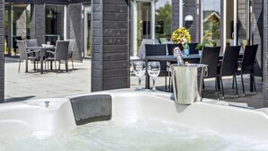 Un espacio exterior moderno con zona de estar, jacuzzi, mesas y sillas para comer.