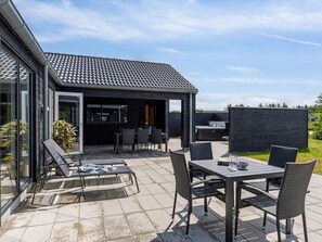 A modern outdoor patio with a dining table and chairs, a hot tub, and a covered seating area. - 5 Star Holiday Home in Norre Nebel (Norre Nebel)