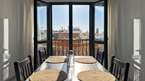 Une table à manger avec quatre chaises, une bouteille et une vue sur le paysage urbain, visible à travers de grandes fenêtres.