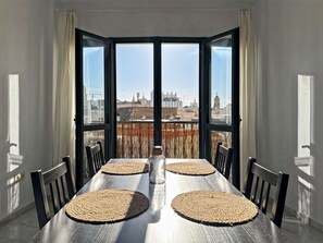 Una mesa de comedor con cuatro sillas, una botella y vistas a un paisaje urbano a través de amplios ventanales.
