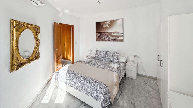 Une chambre à coucher comprenant un lit, une table de chevet, une commode, un miroir, une porte et un tableau accroché au mur.