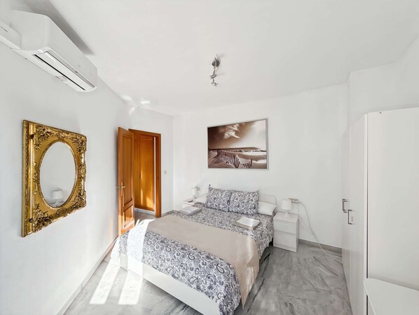 Un dormitorio con cama, mesita de noche, espejo, puerta y un cuadro colgado en la pared.