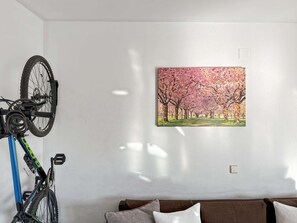 Una habitación con una bicicleta sujeta a un soporte, un cuadro de flores de cerezo en la pared y un sofá marrón.
