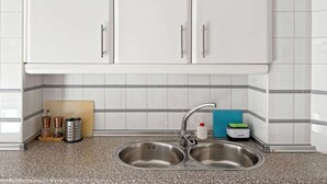 Une cuisine avec des meubles blancs, un évier en acier inoxydable à deux bacs et un plan de travail en granit.