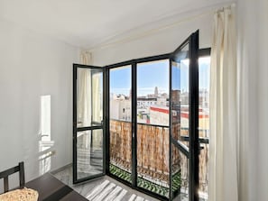 Et værelse med en stor skydedør, der fører ud til en balkon med udsigt over bygninger.