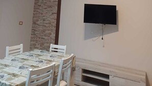 A dining area with a table and chairs, a ceiling fan, and a mounted television. - Summer events agr pt (Torre Melissa)
