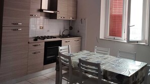 A modern kitchen with light wood cabinets, a gas stove, and a dining area with a table and chairs. - Summer events agr pt (Torre Melissa)