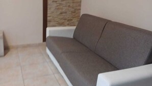 A modern living room with a grey sofa against a textured wall and tiled floor. - Summer events agr pt (Torre Melissa)