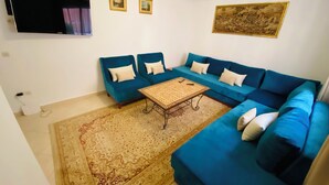 A living room with a blue sofa set, a coffee table, a patterned rug, and a flat-screen TV mounted on the wall. - Quiet modern apartment in Guéliz with parking and wifi (Marrakech)