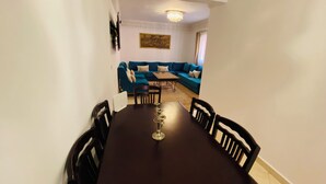 A dining area with a dark wooden table and chairs, a chandelier, and a blue sofa set in the background. - Quiet modern apartment in Guéliz with parking and wifi (Marrakech)