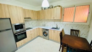 A compact kitchen with wooden cabinets, a built-in oven, a microwave, a washing machine, and a dining area with a table and chairs. - Quiet modern apartment in Guéliz with parking and wifi (Marrakech)
