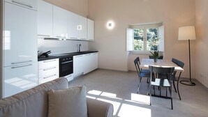 A modern kitchen with white cabinets, a black countertop, and a dining area with a table and chairs. - Campetti (Genoa)