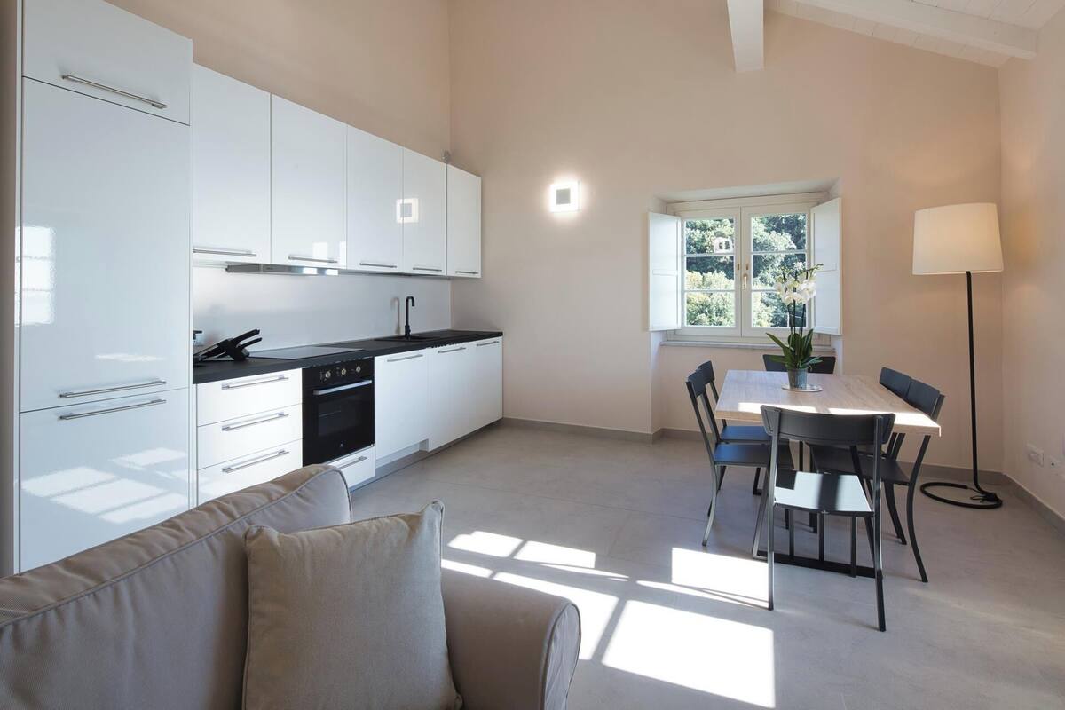 A modern kitchen with white cabinets, a black countertop, and a dining area with a table and chairs.