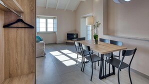 A spacious room with a wooden dining table, black chairs, a sofa, and a TV. - Campetti (Genoa)