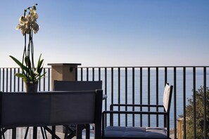 A balcony with a view of the sea, featuring a chair, a table, and a potted plant.