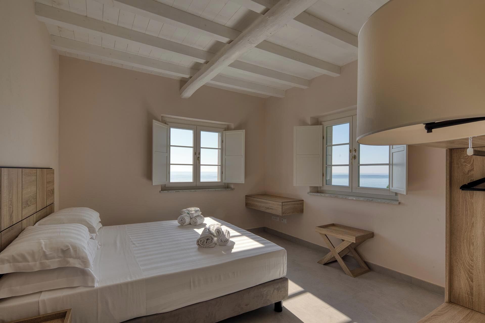 A bedroom with a bed, two windows, a wooden bench, and a hanging coat rack.