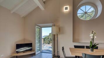 A spacious room with a large window, a dining table, and a flat-screen TV.