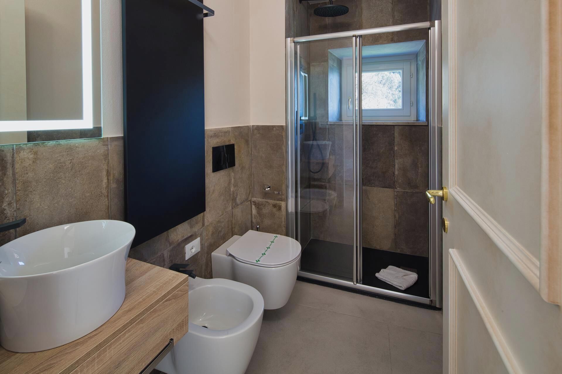 Un baño moderno con un lavamanos grande de color blanco, un bidé y una ducha con cerramiento de vidrio.
