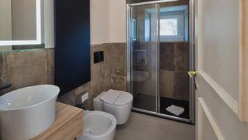 Un baño moderno con un lavamanos grande de color blanco, un bidé y una ducha con cerramiento de vidrio.