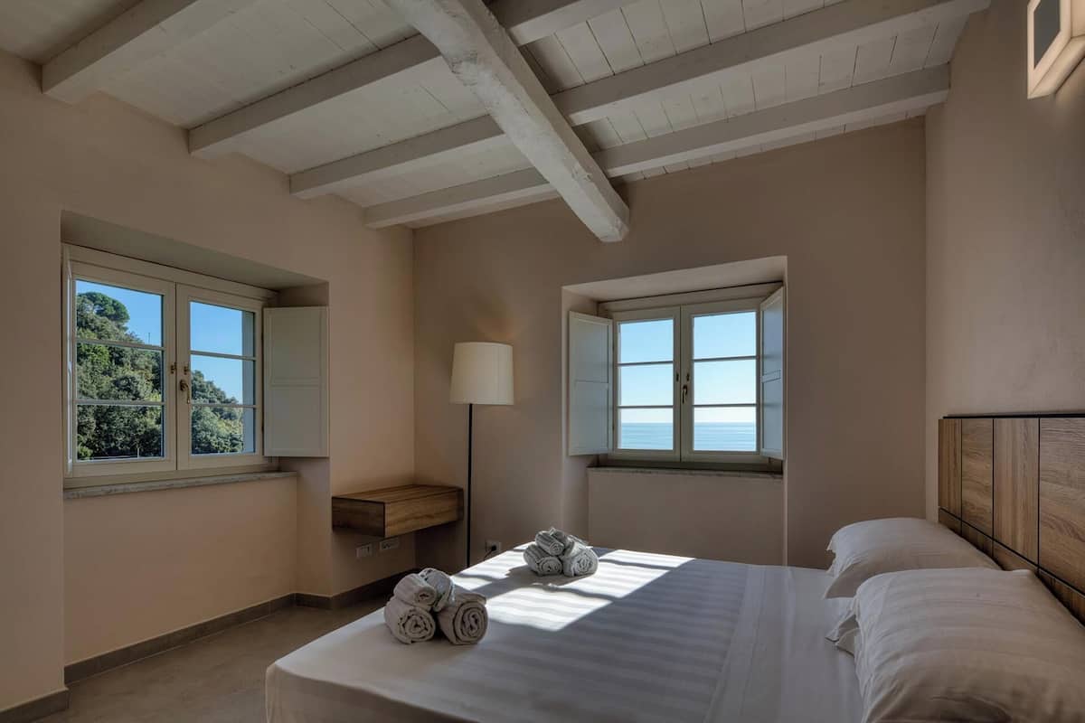 A bedroom with two windows, a bed with white linens, and a wooden bench.